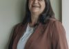 Smiling woman wearing a blazer standing indoors, exuding confidence and warmth.